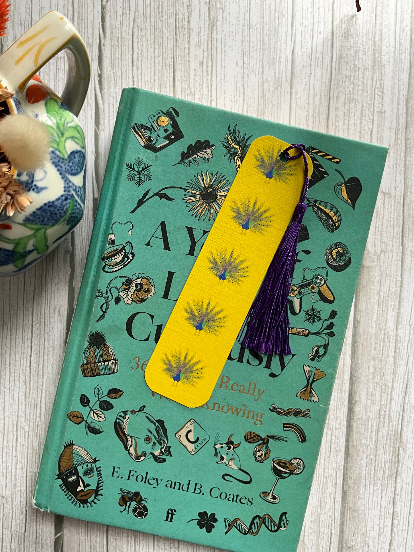 Book with a yellow peacock print bookmark with a navy blue tassel on it. 