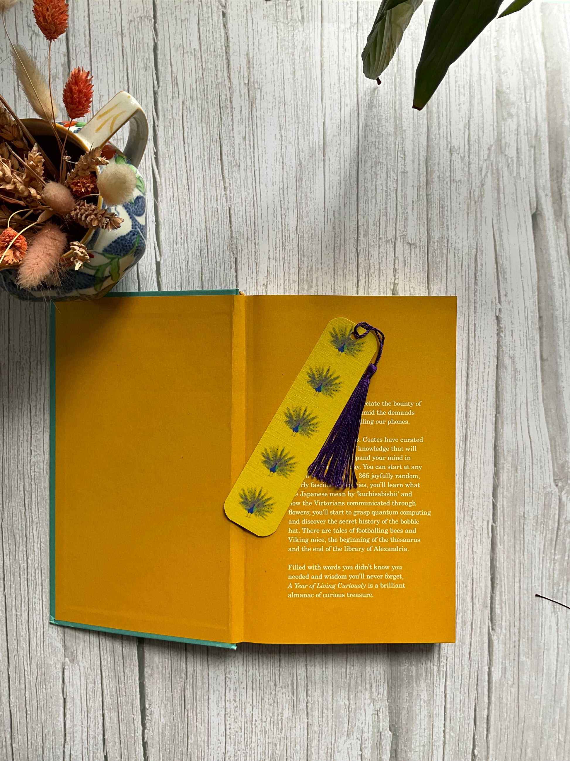 Open book with a yellow bookmark with a illustrated peacock print pattern and a blue tassel.