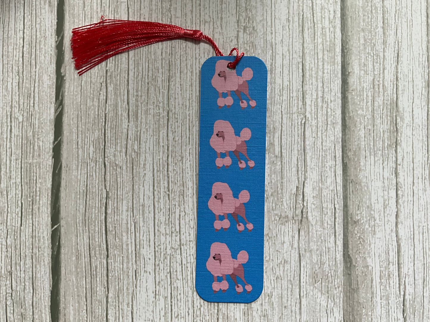 Blue bookmark with pink dog illustrations and a pink tassel on a wooden surface