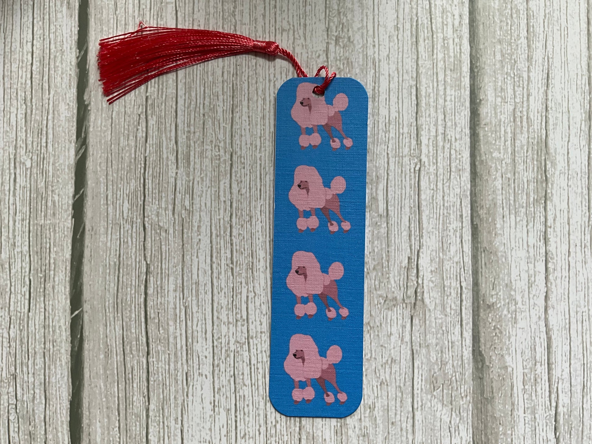 Blue bookmark with pink dog illustrations and a pink tassel on a wooden surface