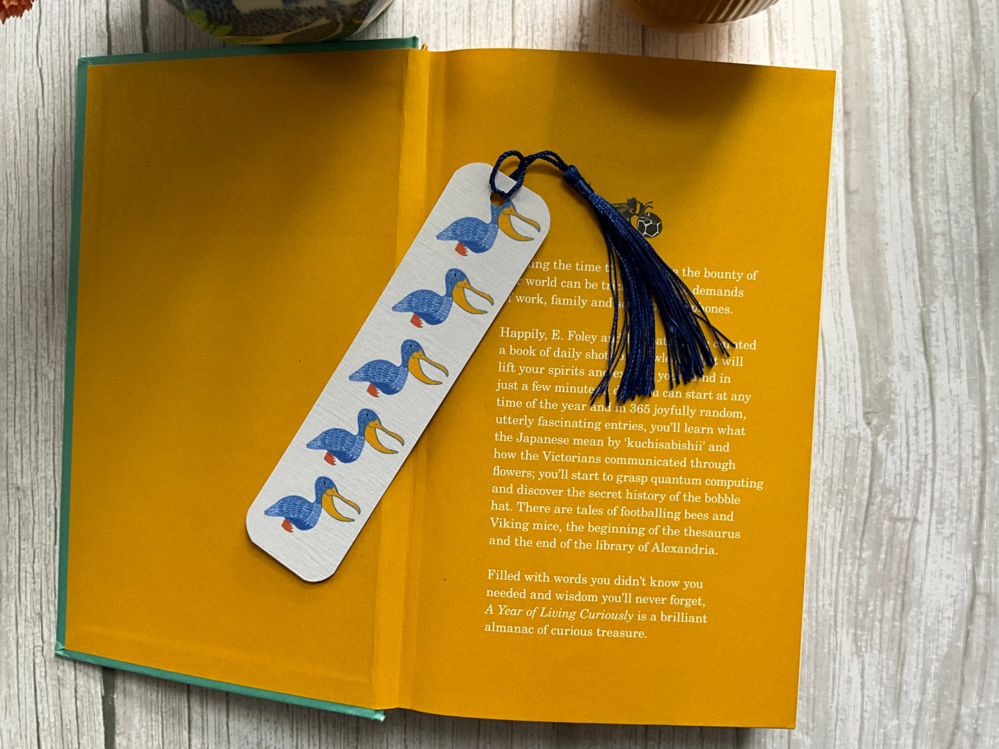 Book with a decorative blue pelican bookmark and blue tassel resting on a wooden surface