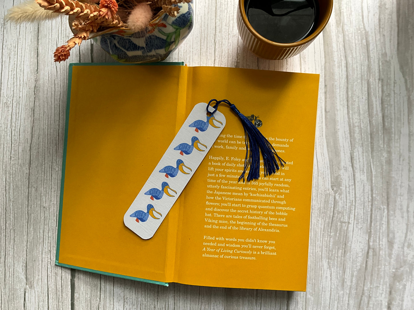 Open book with a bookmark featuring hand illustrations of blue pelicans on a wooden surface.
