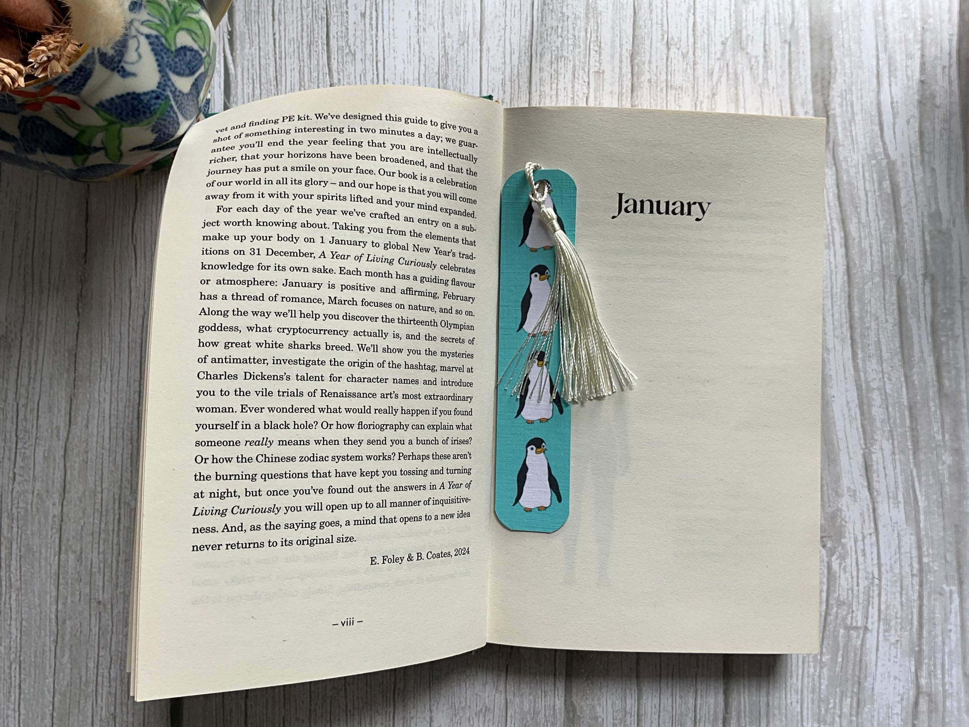 Open book with a decorative bookmark featuring penguins on a wooden surface.