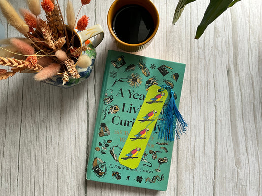 Green book with colorful bookmark, cup of coffee, and dried flowers on a wooden surface
