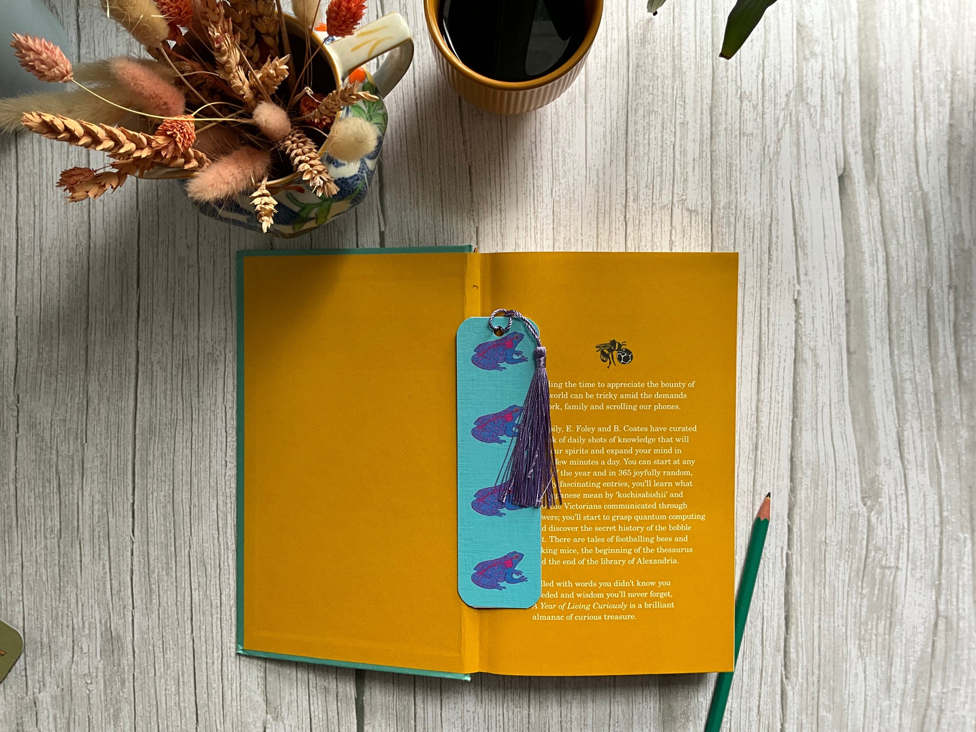Open book with a colorful bookmark on a wooden surface with a cup and flowers.