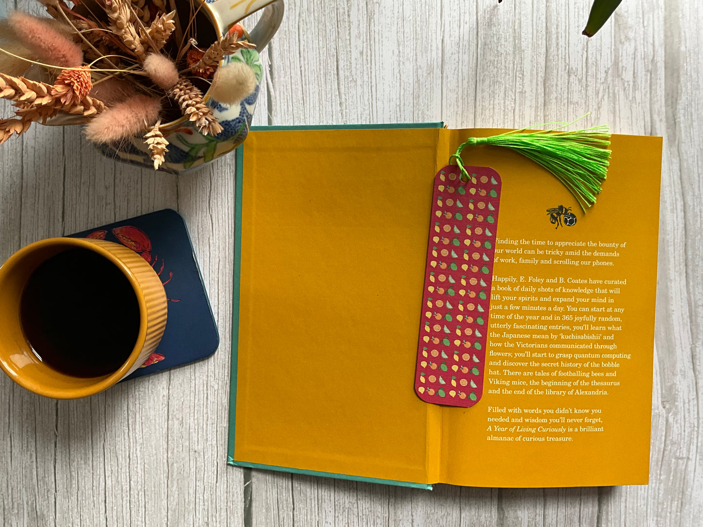 Open book with a colorful bookmark on a wooden surface next to a cup of coffee and decorative elements.