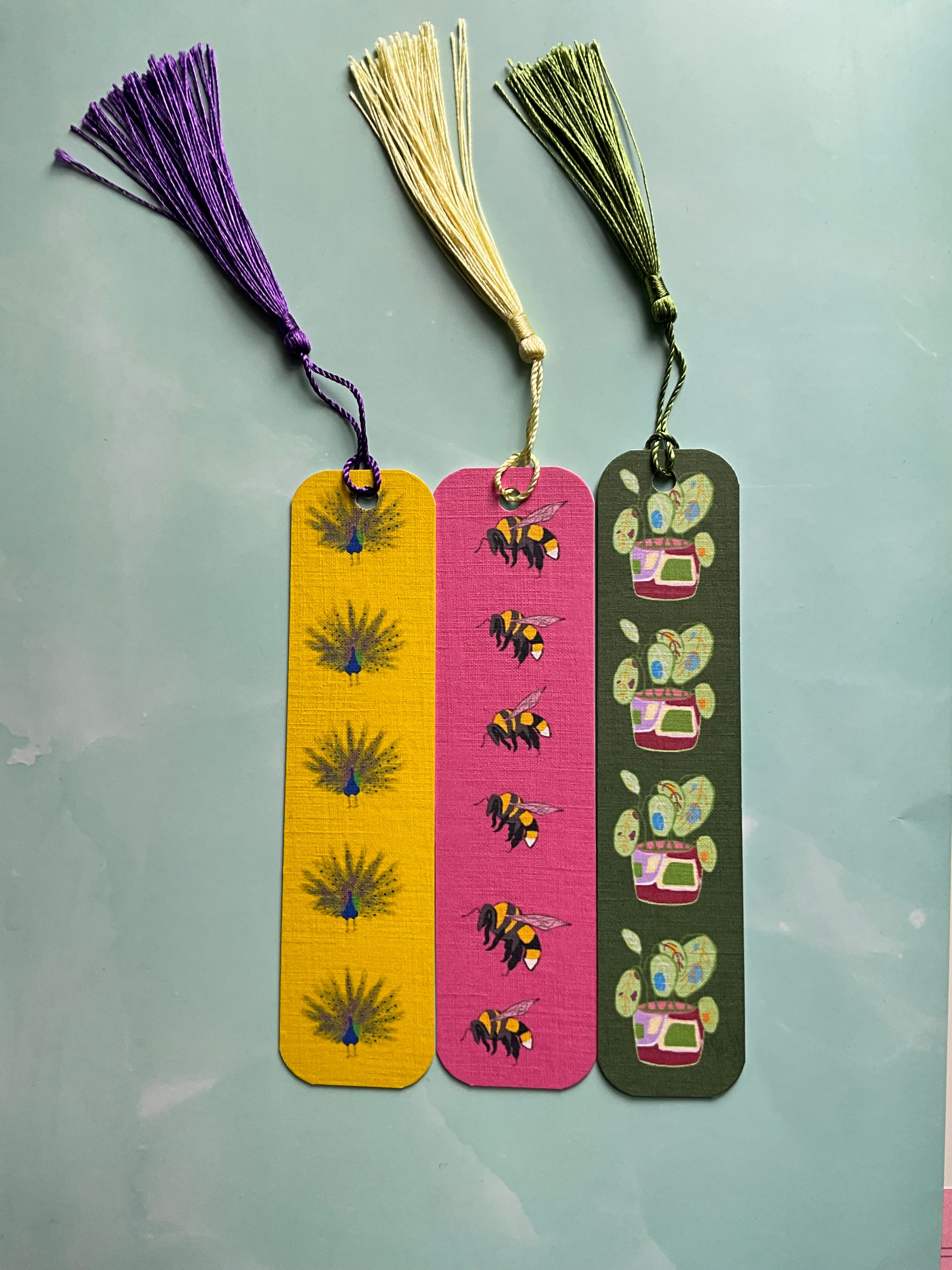 Three nature themed bookmarks with colourful tassels on a blue marble background