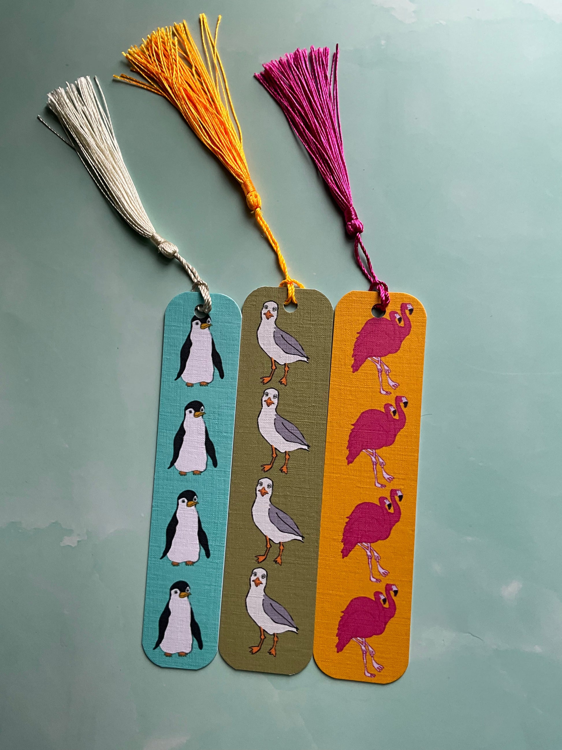 Three colorful bookmarks with bird designs and bright tassels on a light blue background