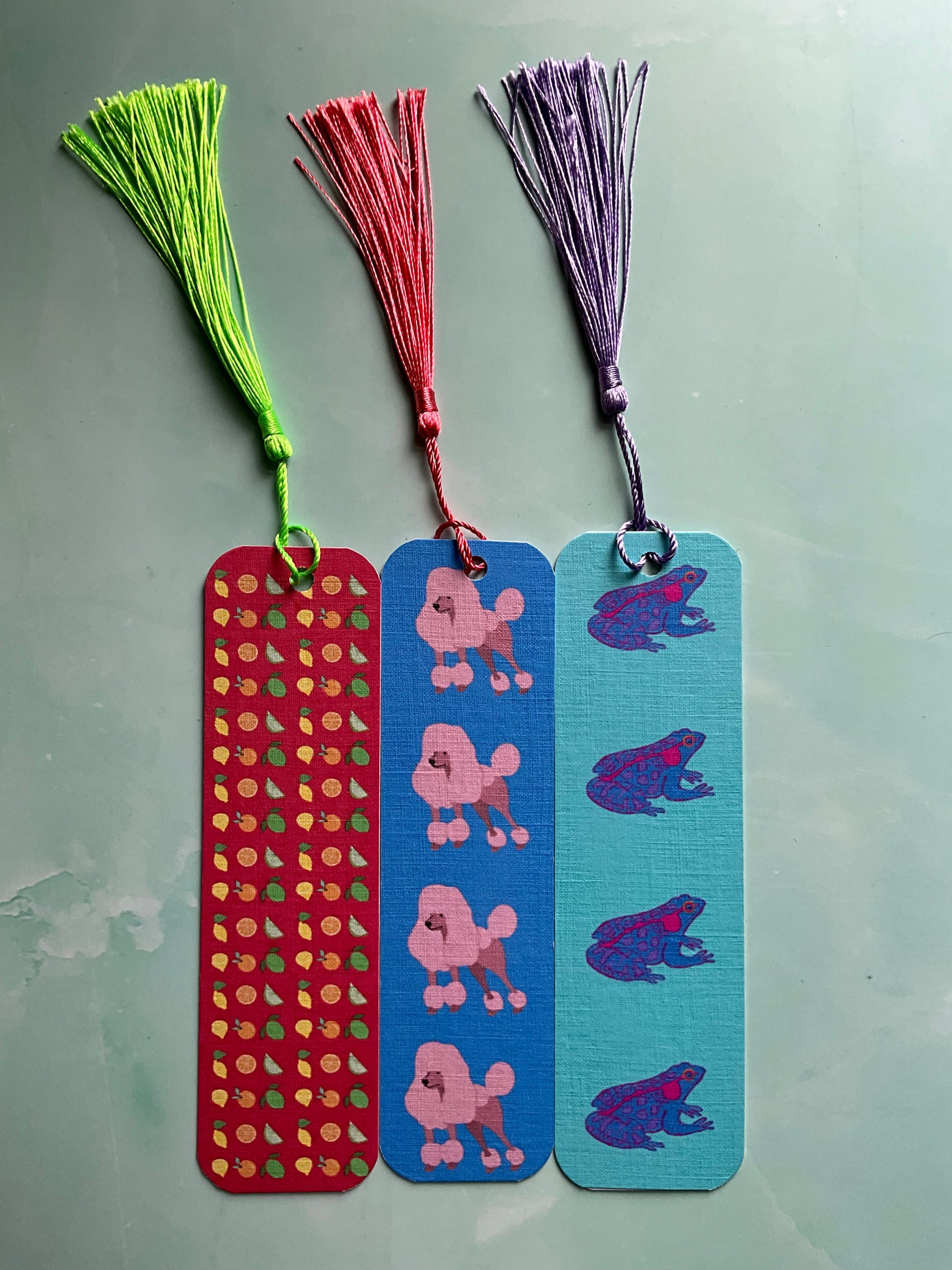 Three colourful, handmade bookmarks with tassels on a blue marble background