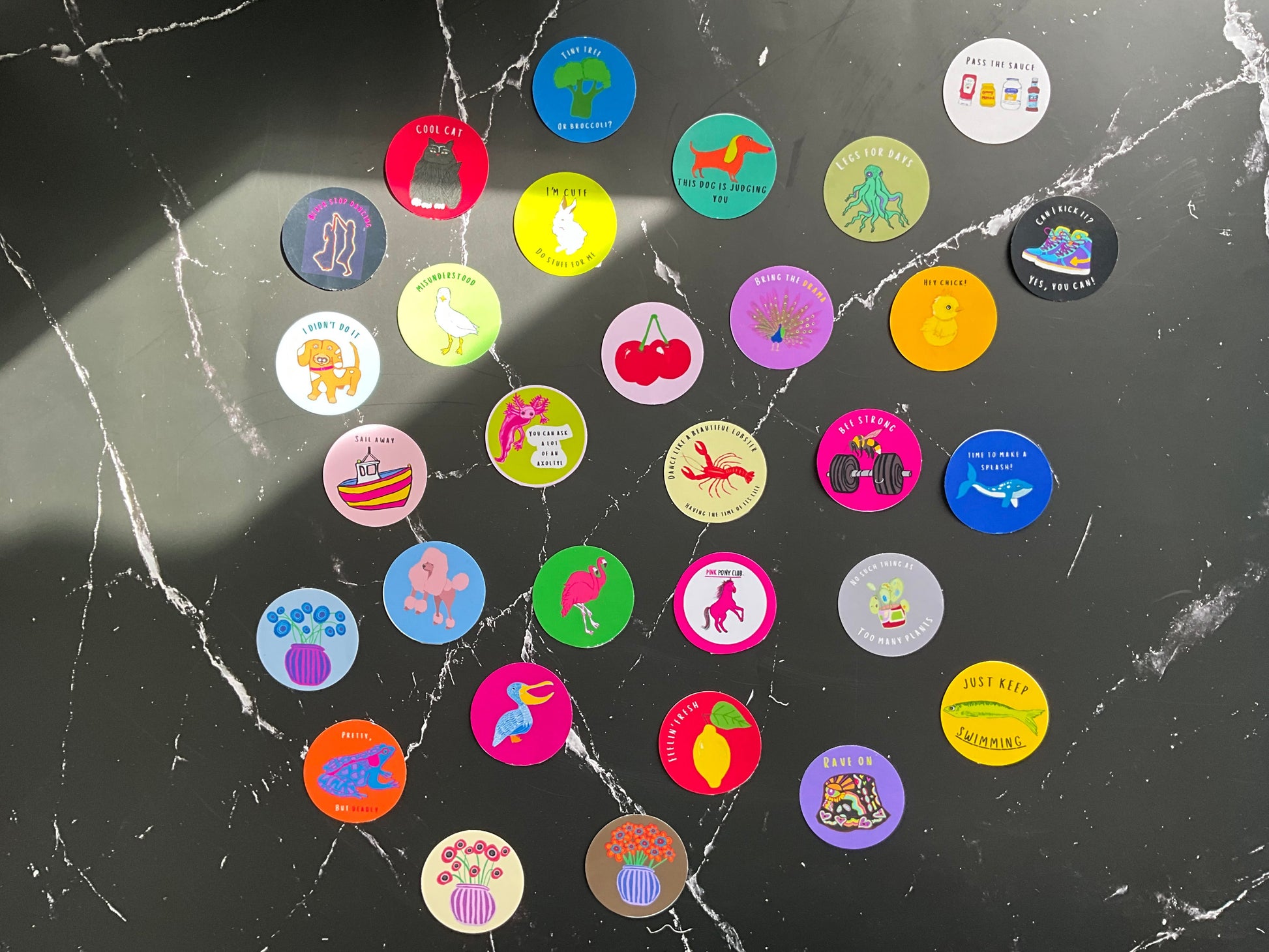 Collection of colorful round stickers on a black surface with visible cracks.