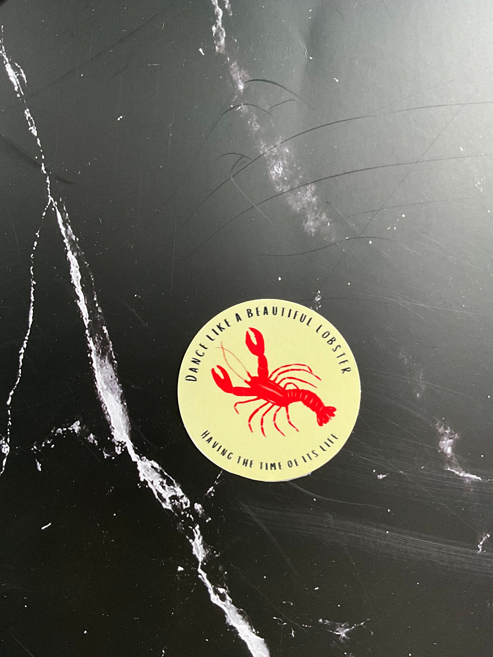 Round cream vinyl sticker featuring an illustration of a lobster with the phrase ‘dance like a beautiful lobster, having the time of its life’