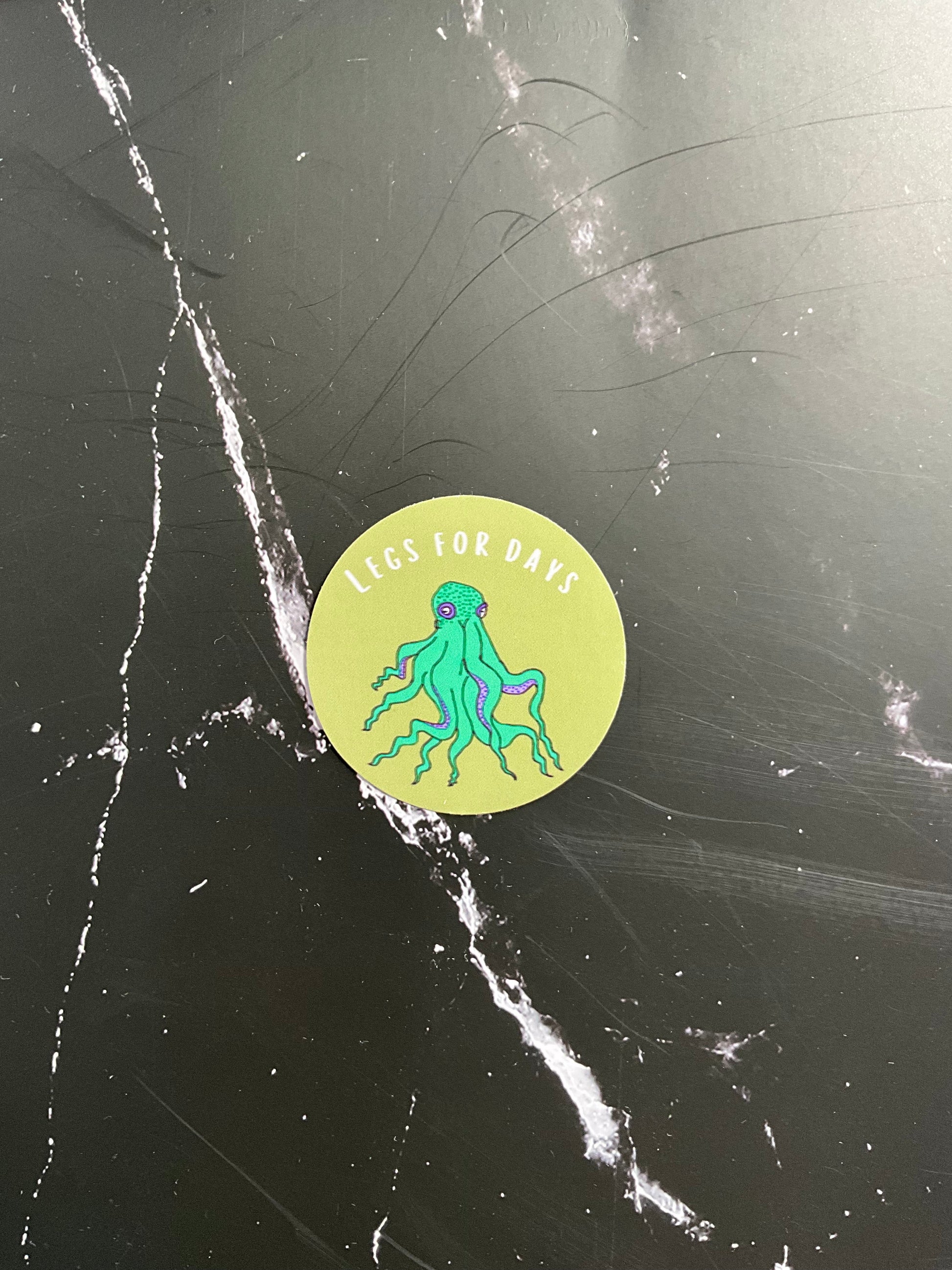 Round sticker with a green octopus design on a black surface