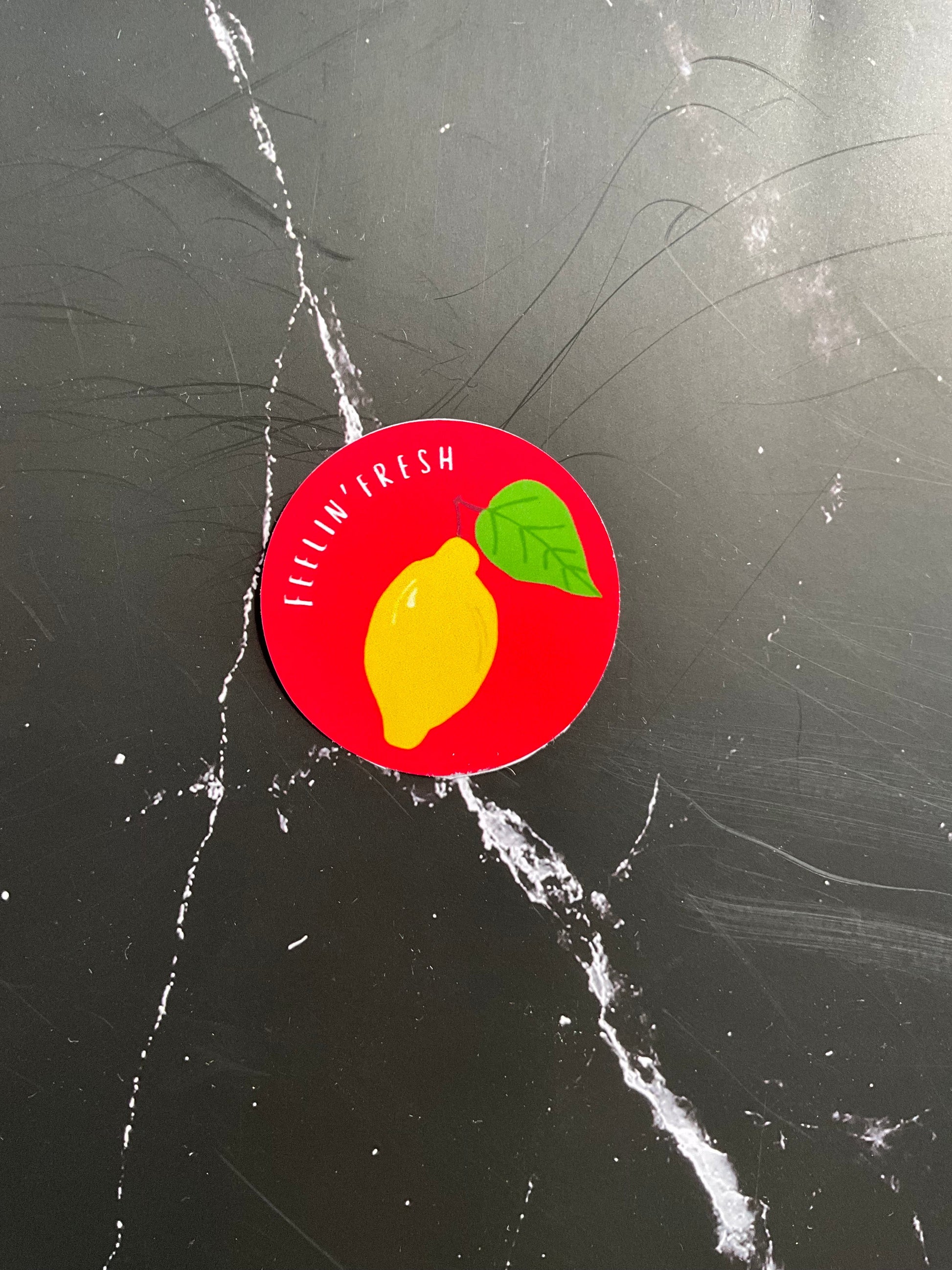 Round red sticker with a lemon graphic on a black marble surface