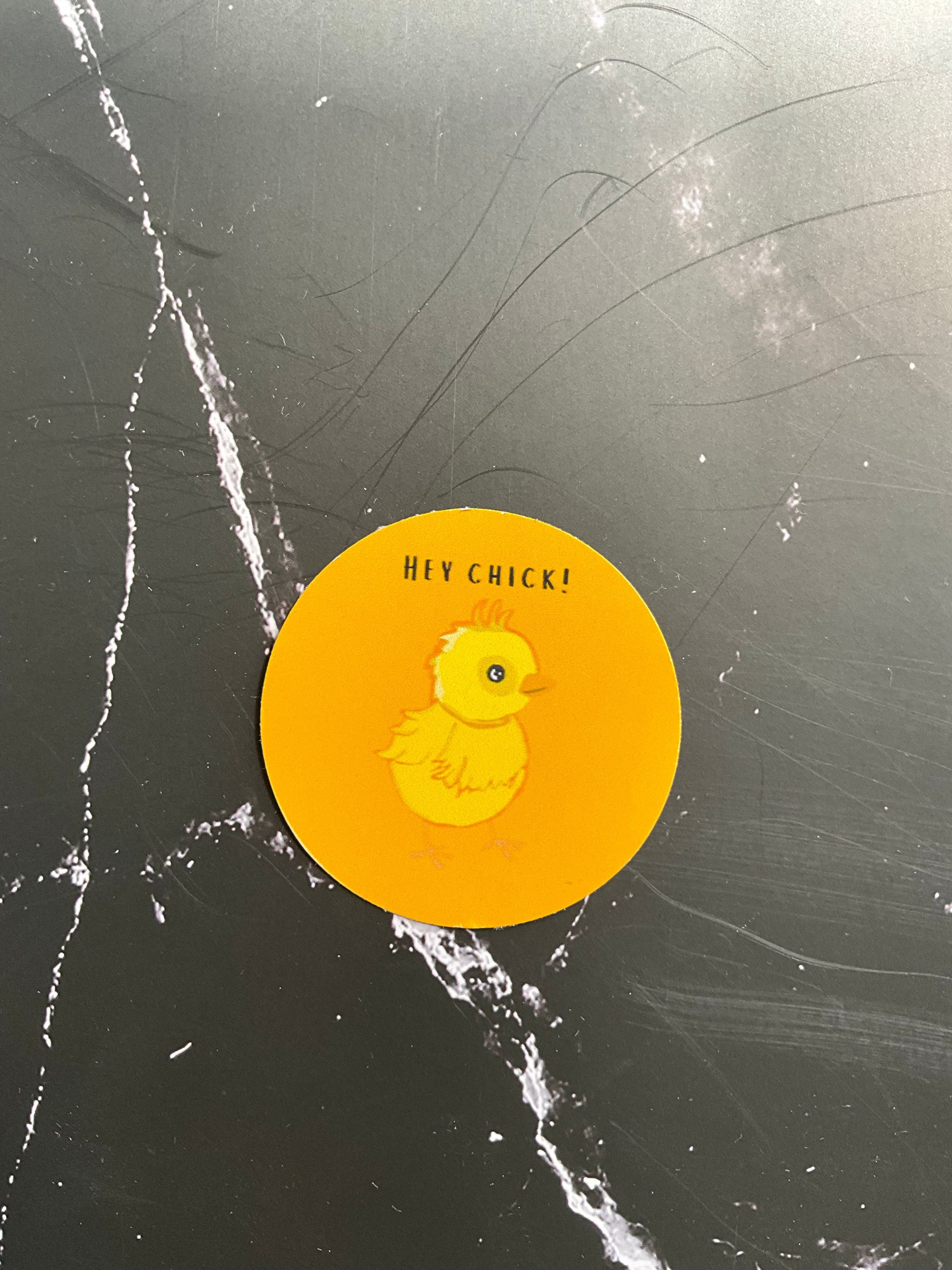Yellow round vinyl sticker featuring a cute chick illustration and the words ‘HEY CHICK!’ In black letters