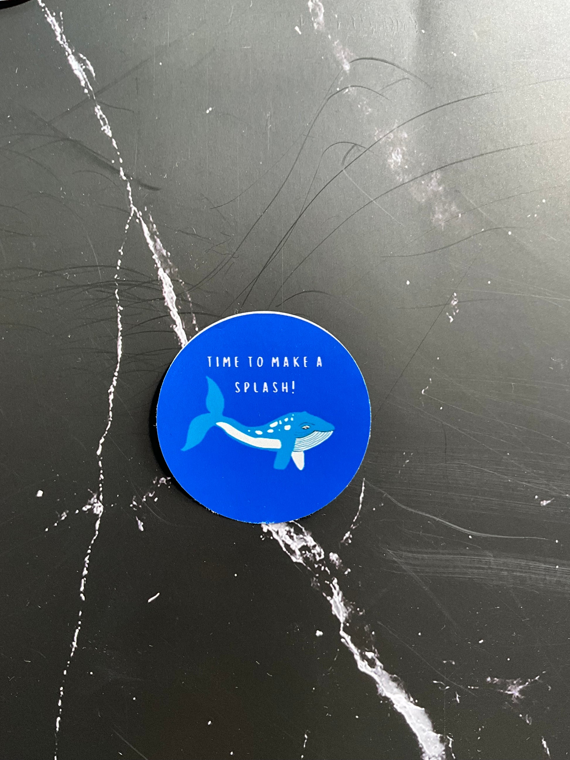 Blue circular sticker with a whale design and text on a scratched black surface