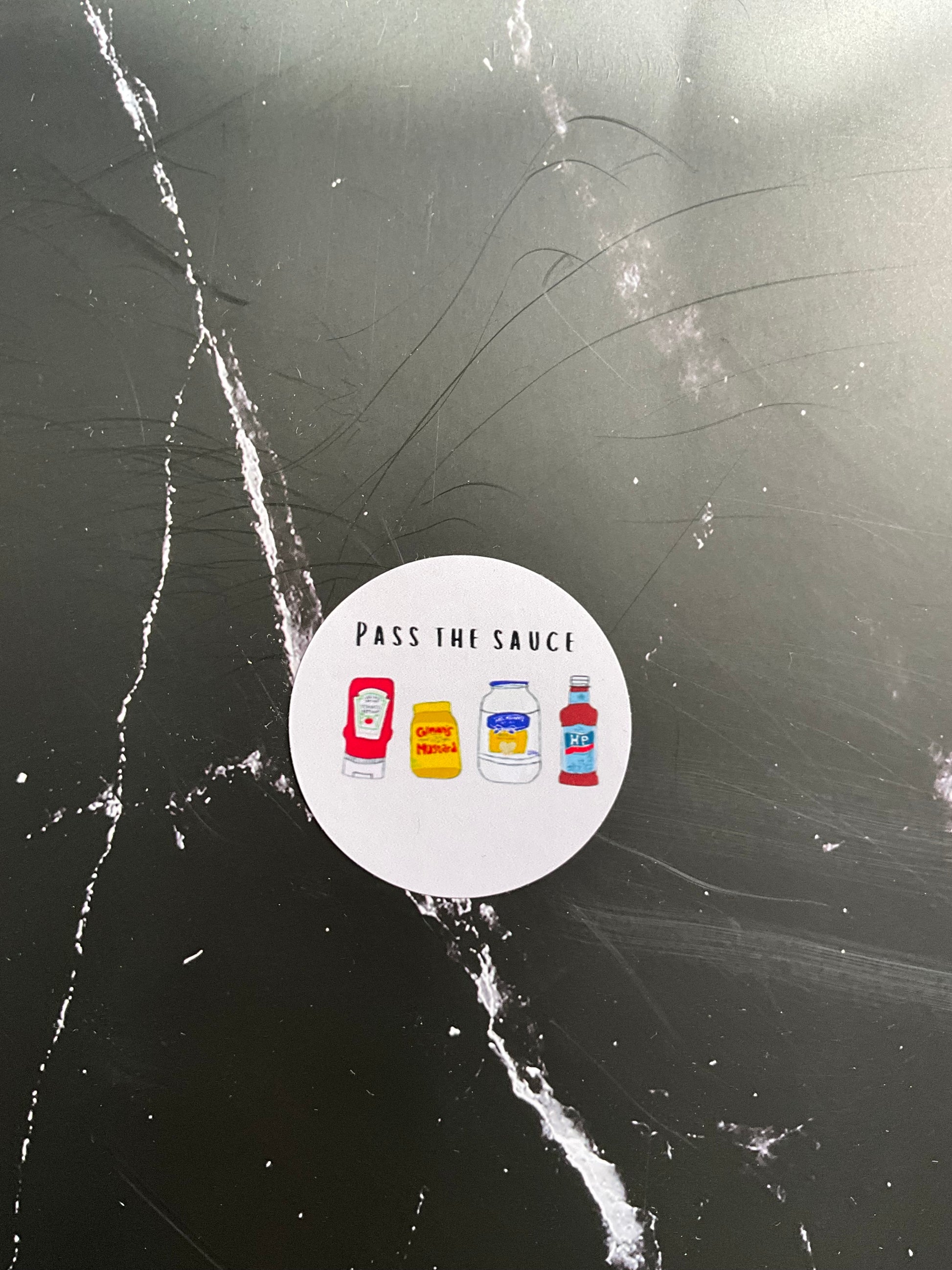 Round sticker with illustrations of sauce bottles on a black marble surface