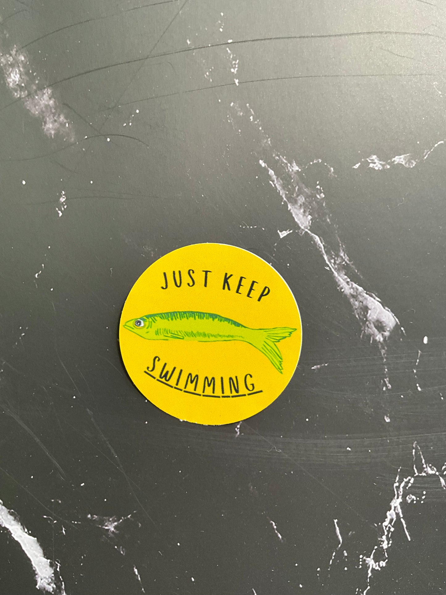 Yellow circular sticker with a fish illustration and text on a black marbled background