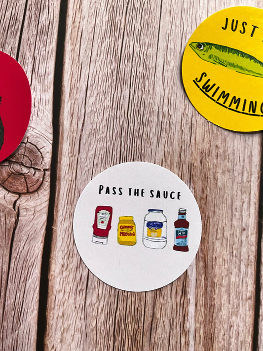 Round vinyl stickers, one with illustration of sauce condiment bottles and text “pass the sauce” on a wooden surface