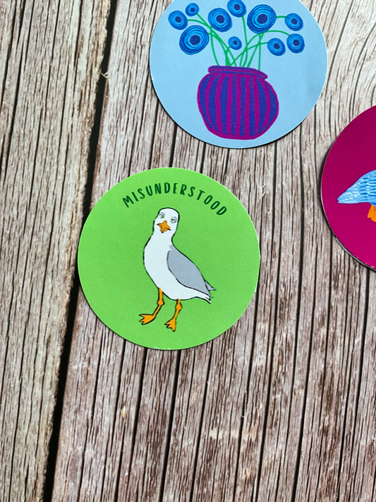 A round green vinyl sticker with a seagull design and the word ‘misunderstood’