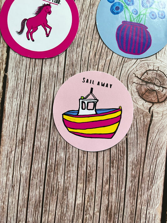 Round vinyl sticker featuring a colourful pink and yellow boat and the words ‘sail away’ in black letters.