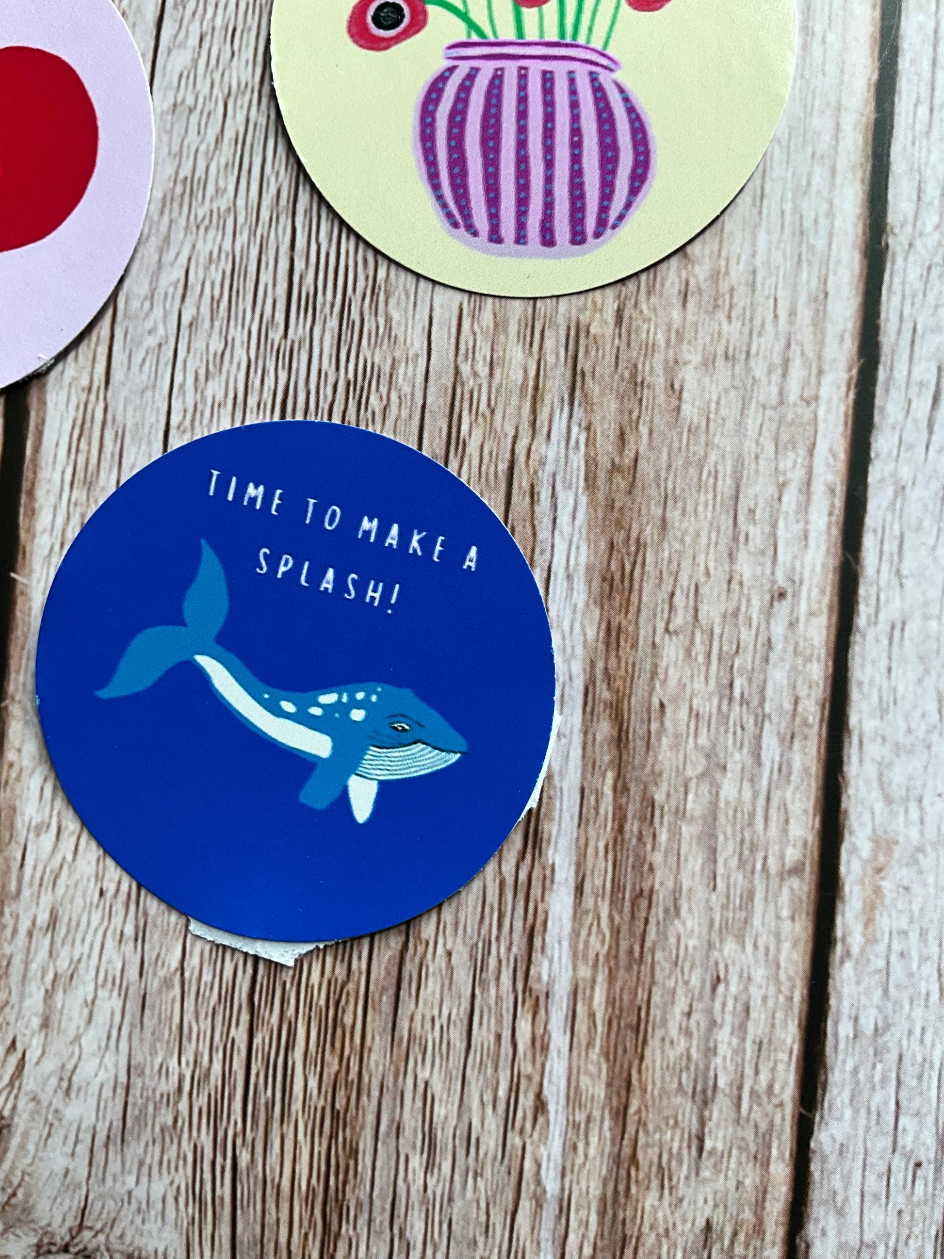 Round blue sticker with a blue whale design and text 'Time to make a splash!' on a wooden surface.
