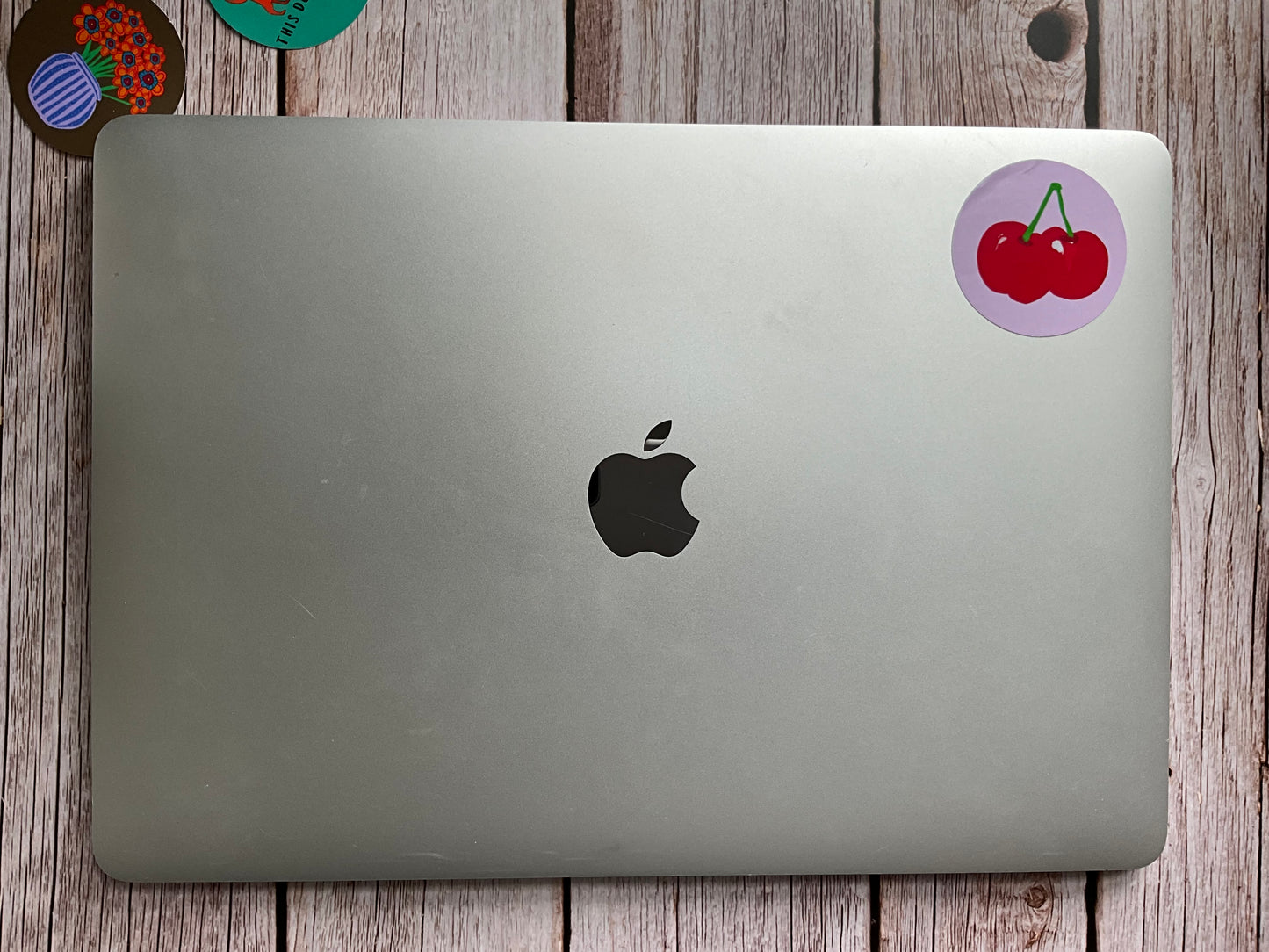 Silver laptop with Apple logo on a wooden surface featuring a cherry sticker in the corner