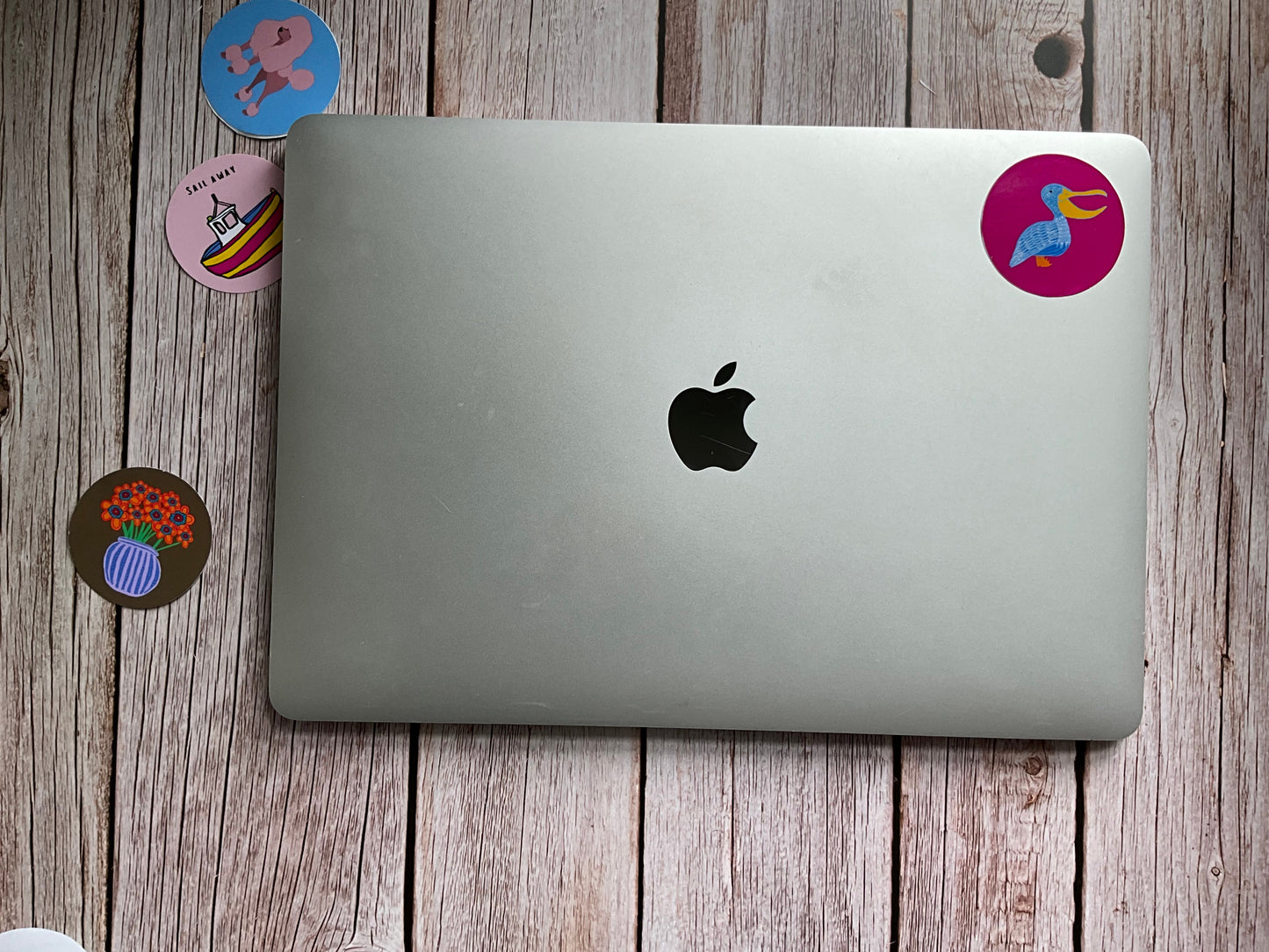 Silver laptop with Apple logo on a wooden surface with colorful stickers.