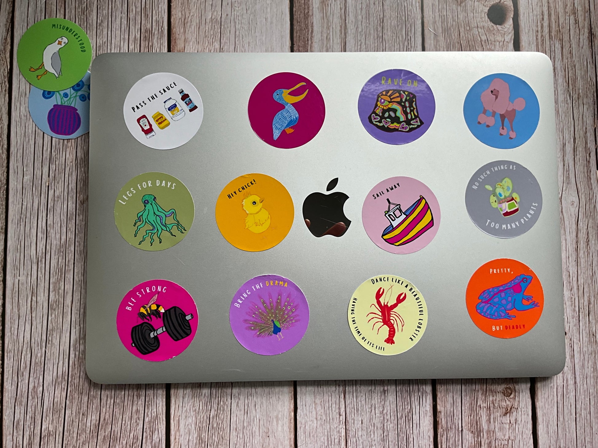 Laptop with various bright, hand-illustrated round vinyl stickers on a wooden surface