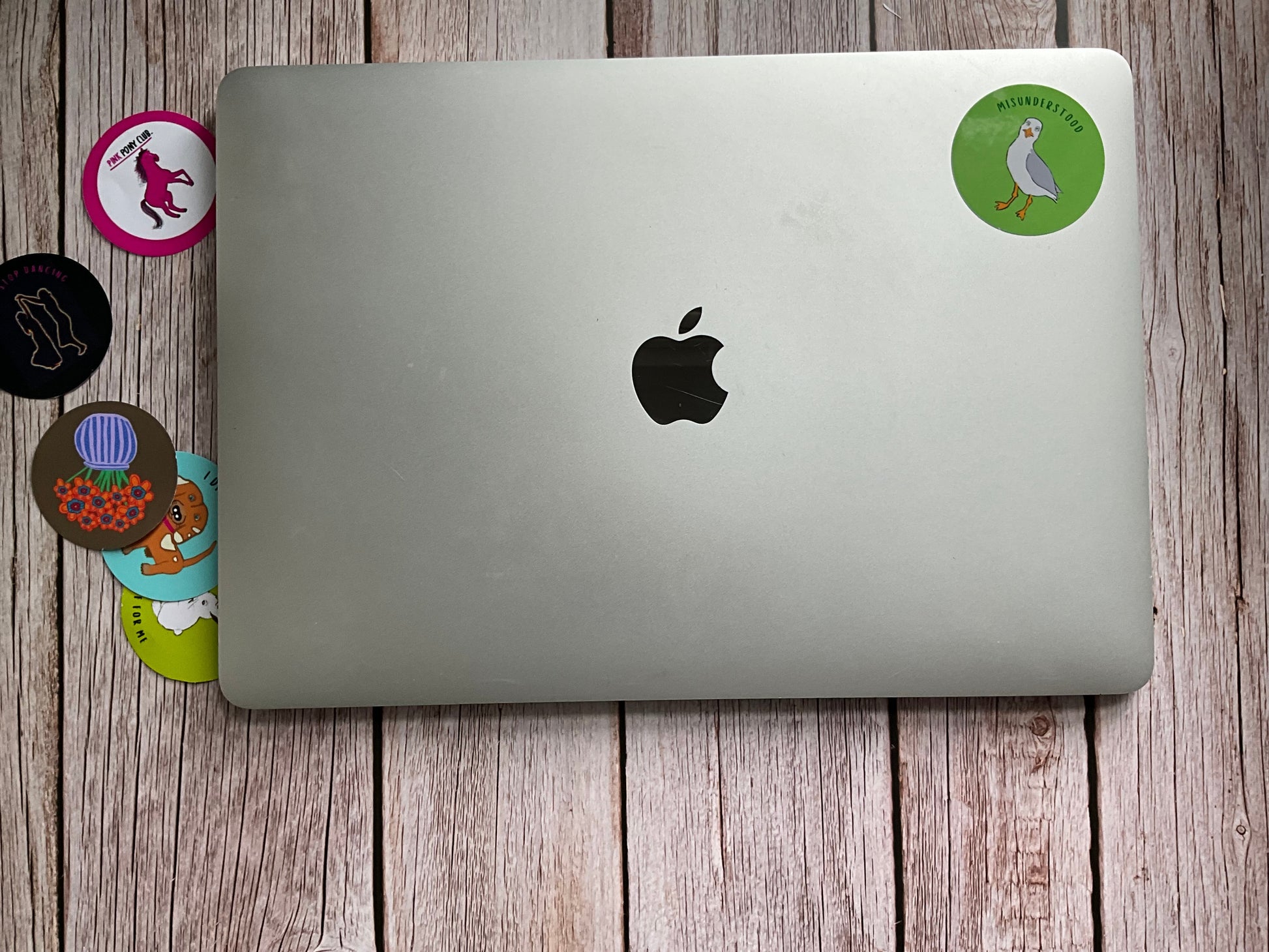 Silver laptop with Apple logo on a wooden surface with stickers around it
