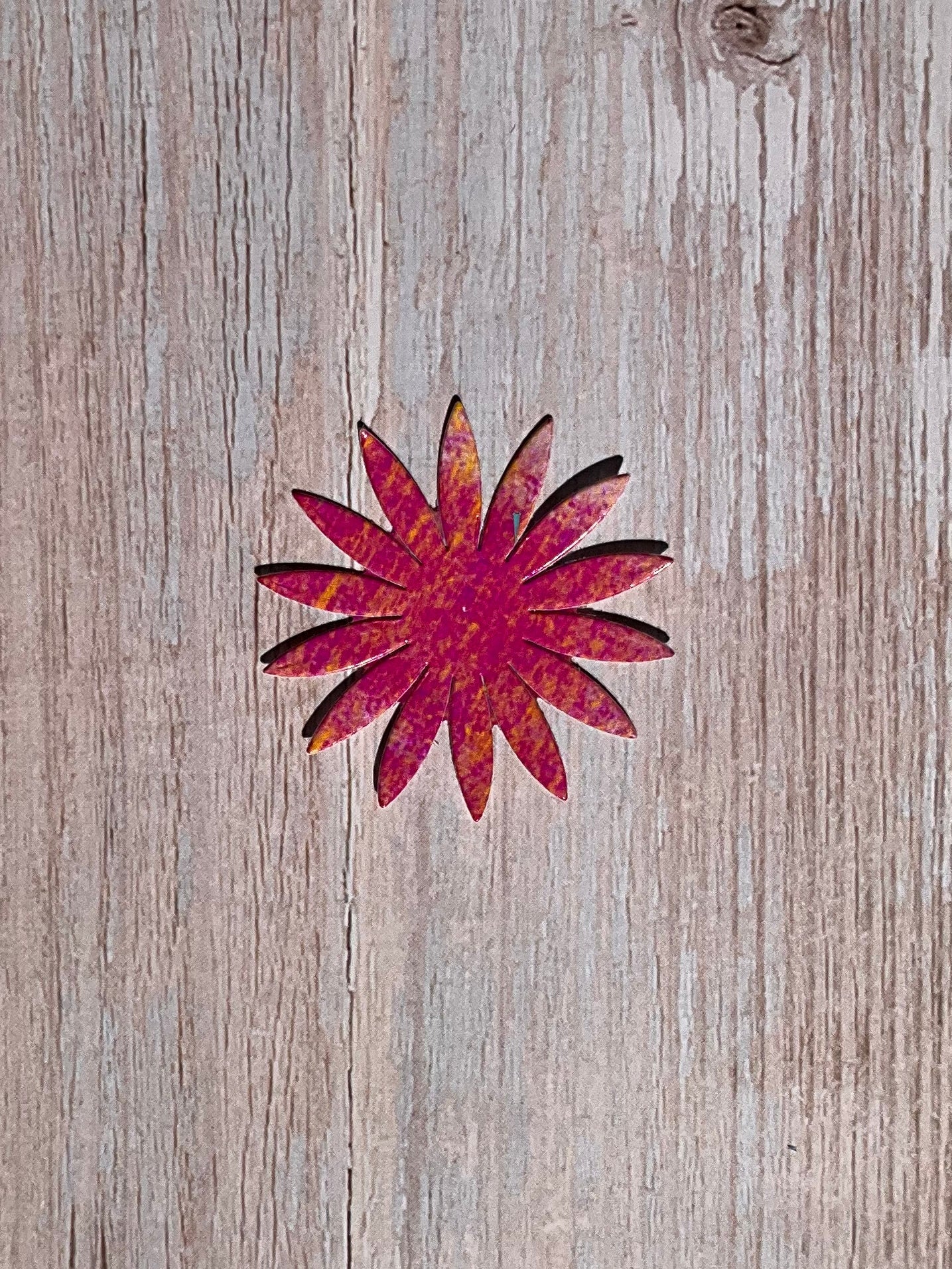 Pink and orange vinyl sticker in the shape of a sunflower, on wood.