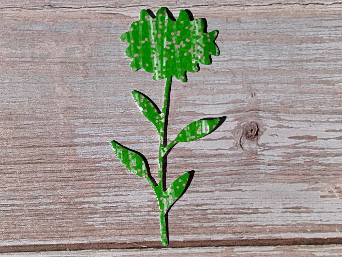 Green patterned vinyl sticker shaped like a sunflower on a wooden background