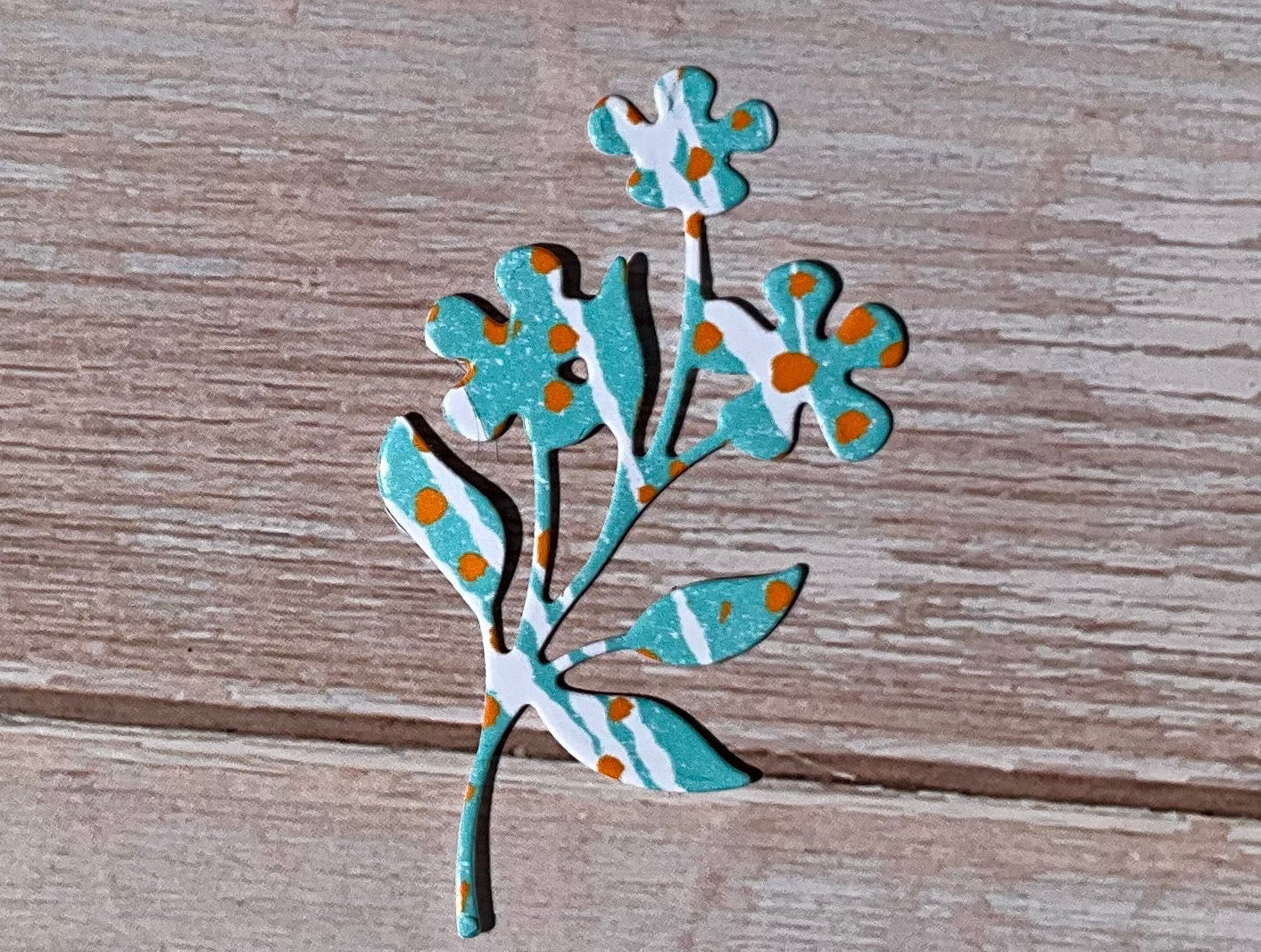 Blue and white striped botanical vinyl sticker with orange spots.  On a wooden background. 