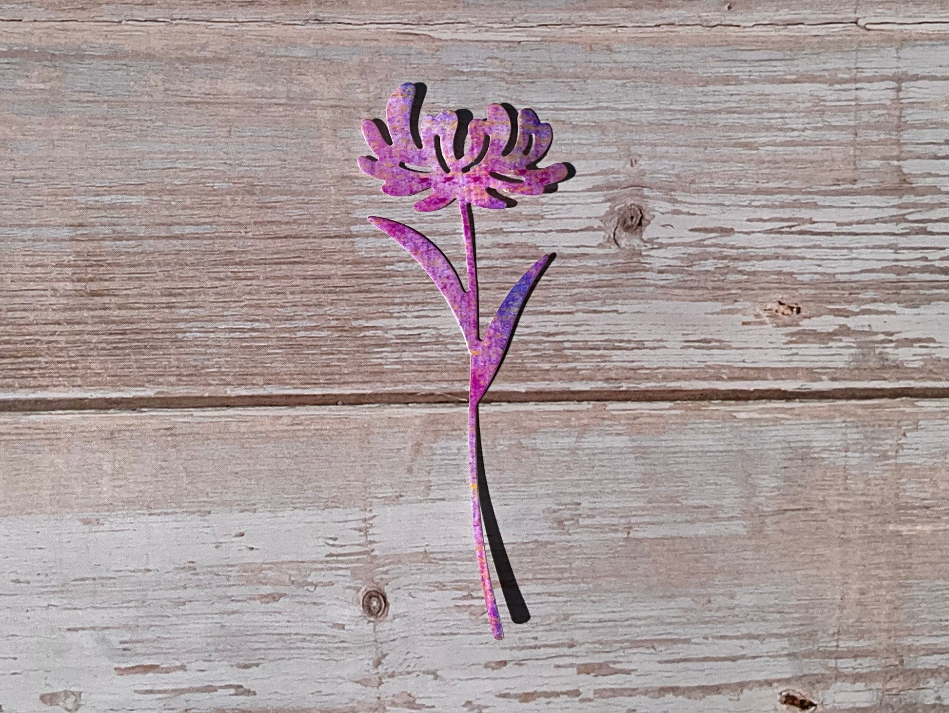 Pink and purple die cut vinyl sticker in the shape of a dandelion on a wooden background