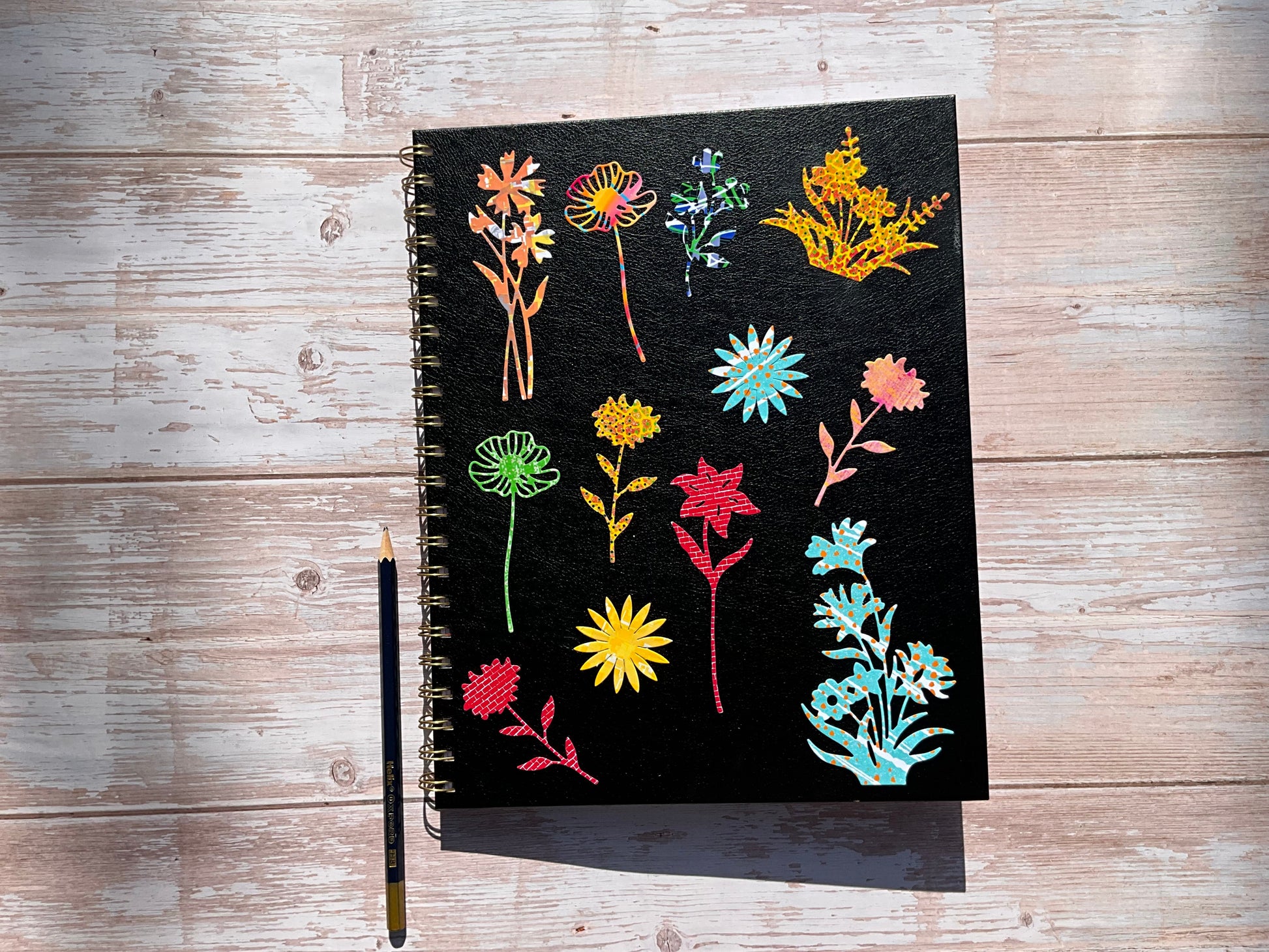 Black notebook with colourful floral sticker designs on a wooden surface