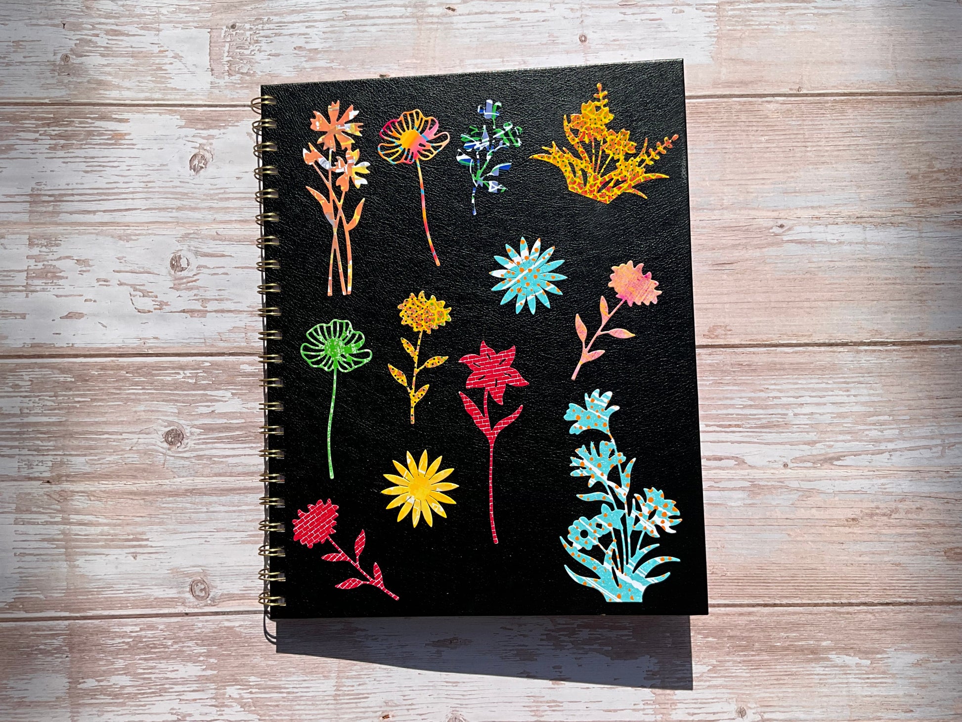 Black notebook with vibrant floral sticker designs on a wooden surface