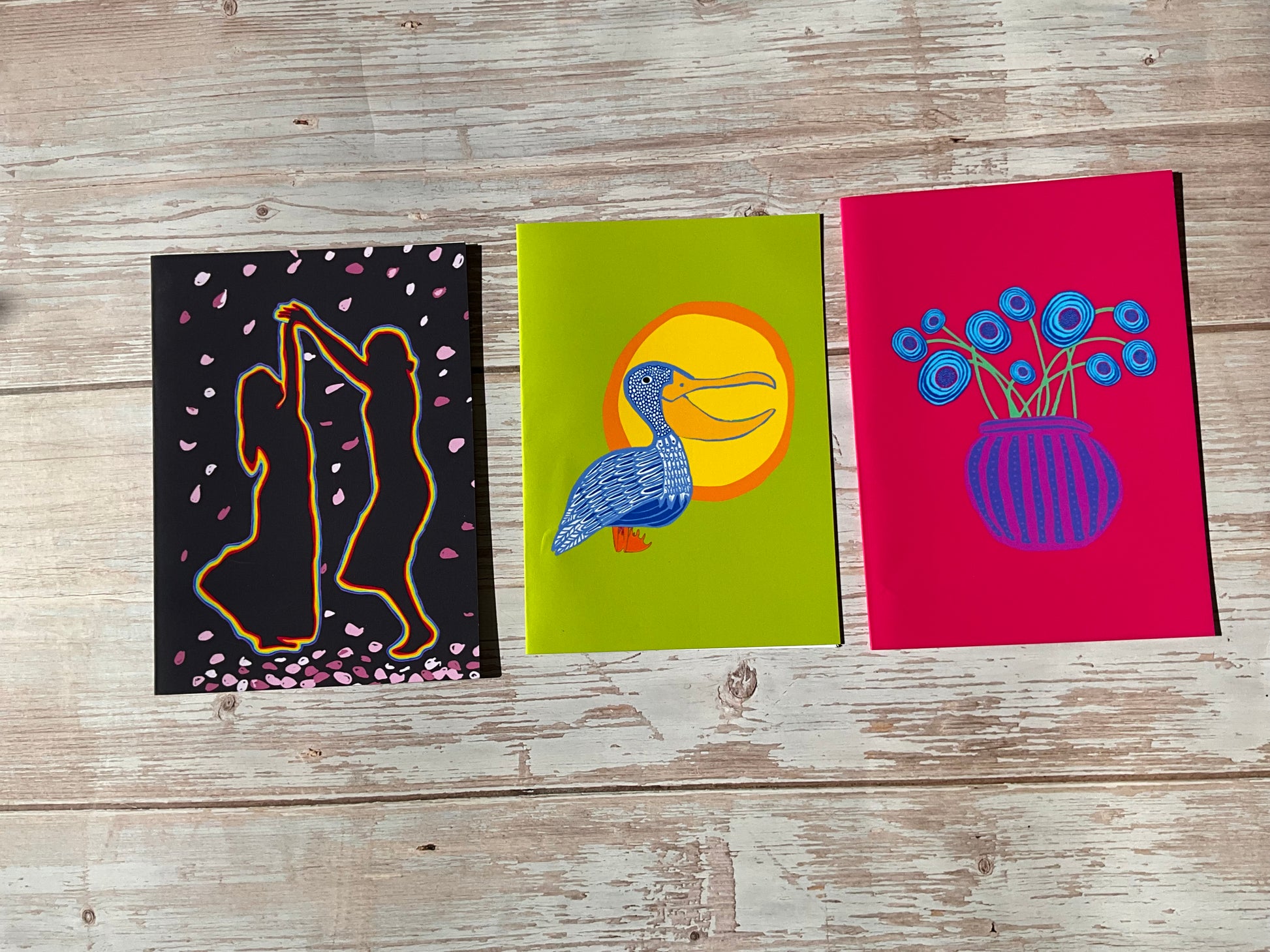 Three colorful greeting cards with artistic designs on a wooden surface