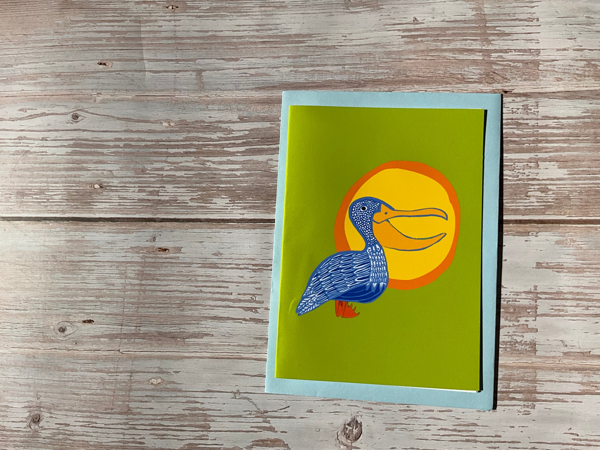 Card with a pelican design on a wooden surface