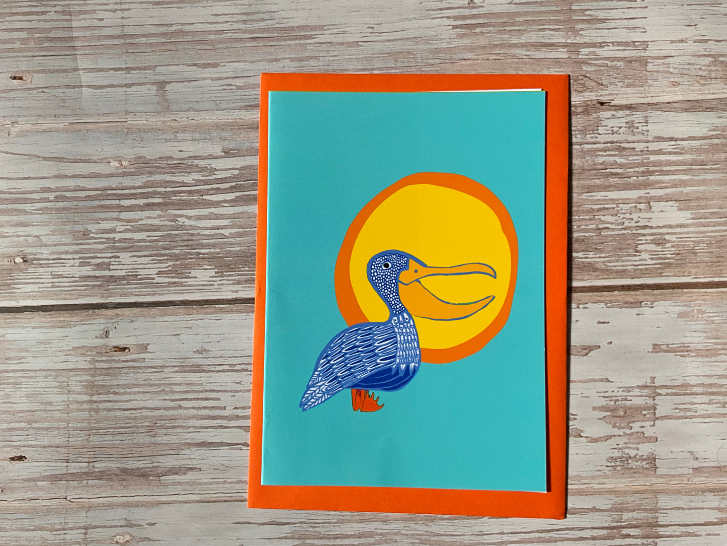 Card with a blue bird illustration on a yellow circle against a teal background, framed by an orange border, on a wooden surface.