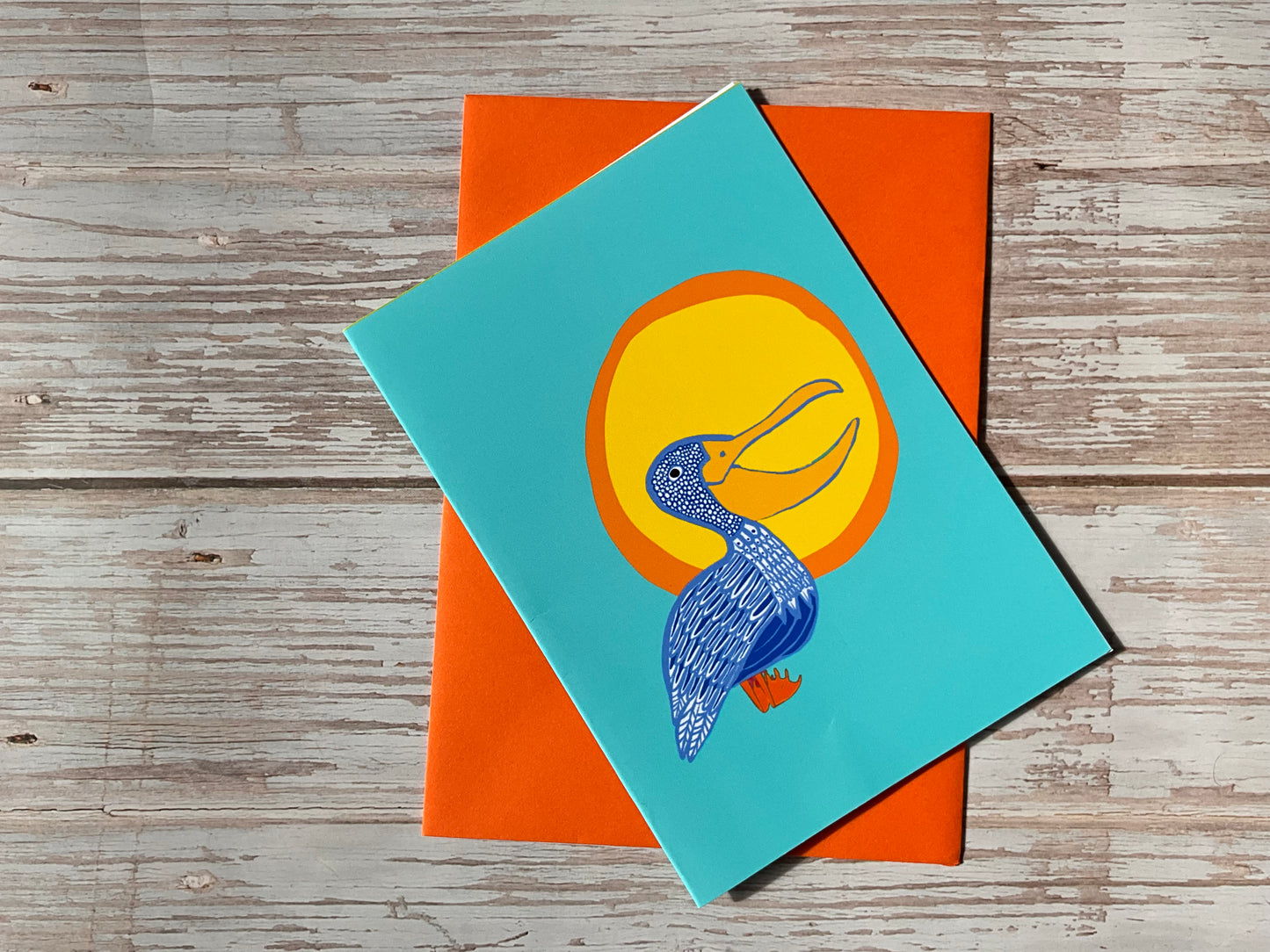 Blue pelican design greetings card with an orange envelope behind it