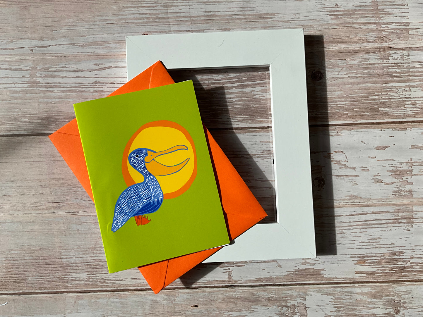Hand-illustrated pelican greeting card with yellow sunshine and lime green background, available as a framed mini print