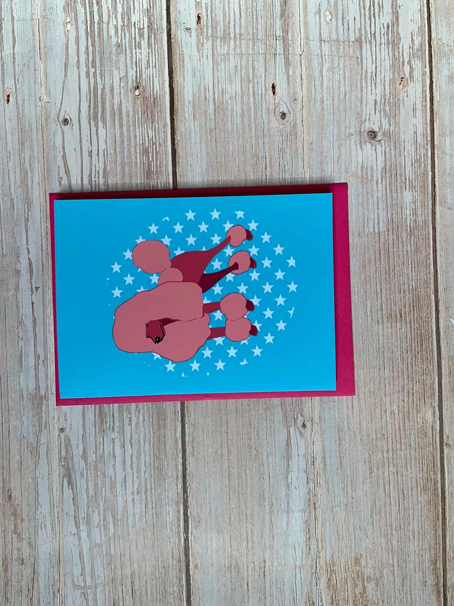 Card with a pink poodle design on a blue background, placed on a wooden surface.