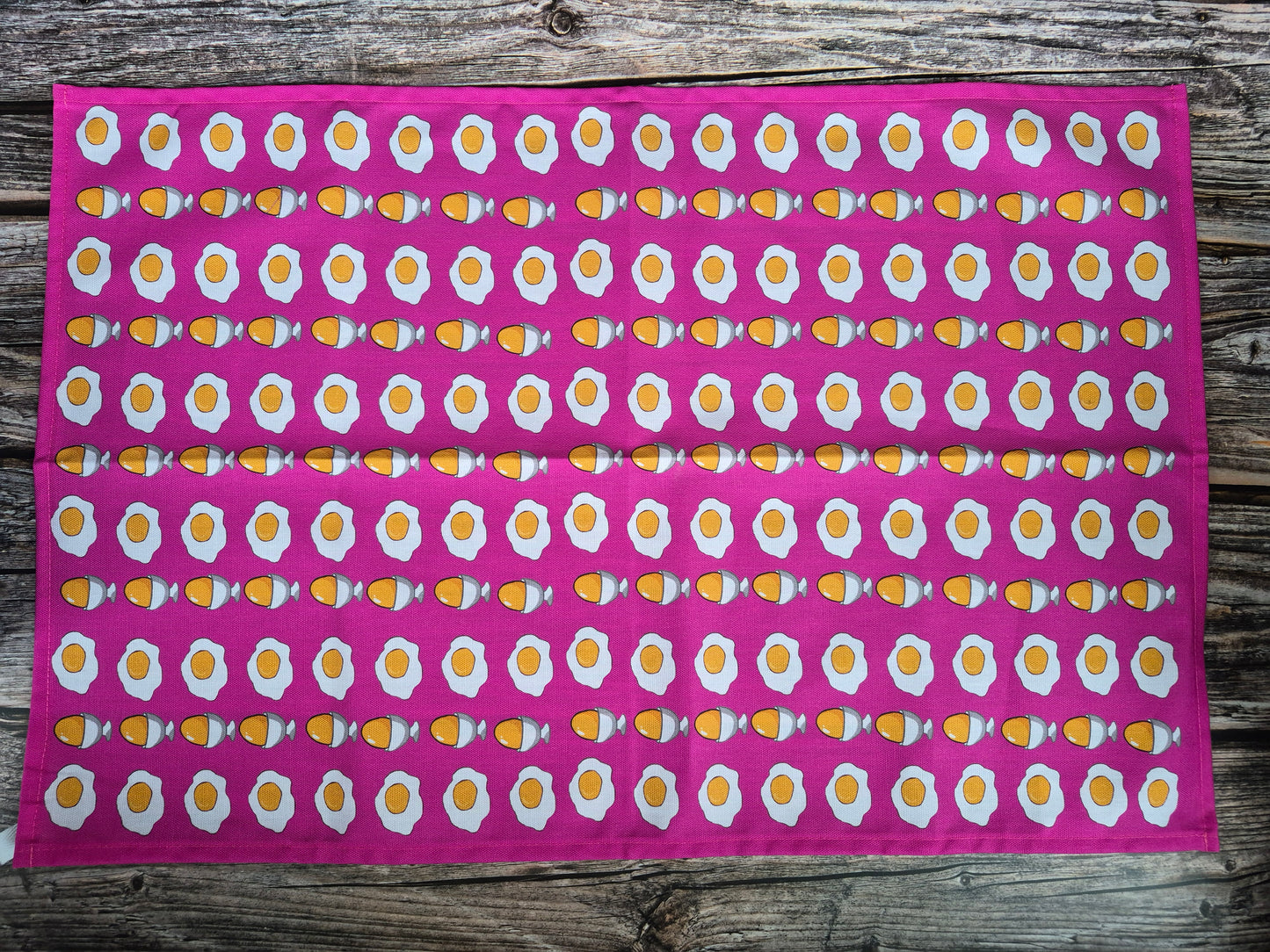 Pink tea towel with egg pattern print on a wooden background