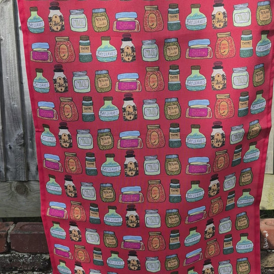 A video of a red tea towel with a illustrated printed design hanging on a washing line flowing in the breeze